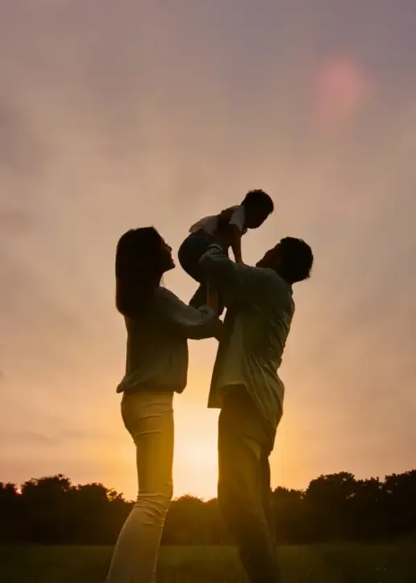 Mother and father holding their baby up in the air against a vibrant sunset sky
